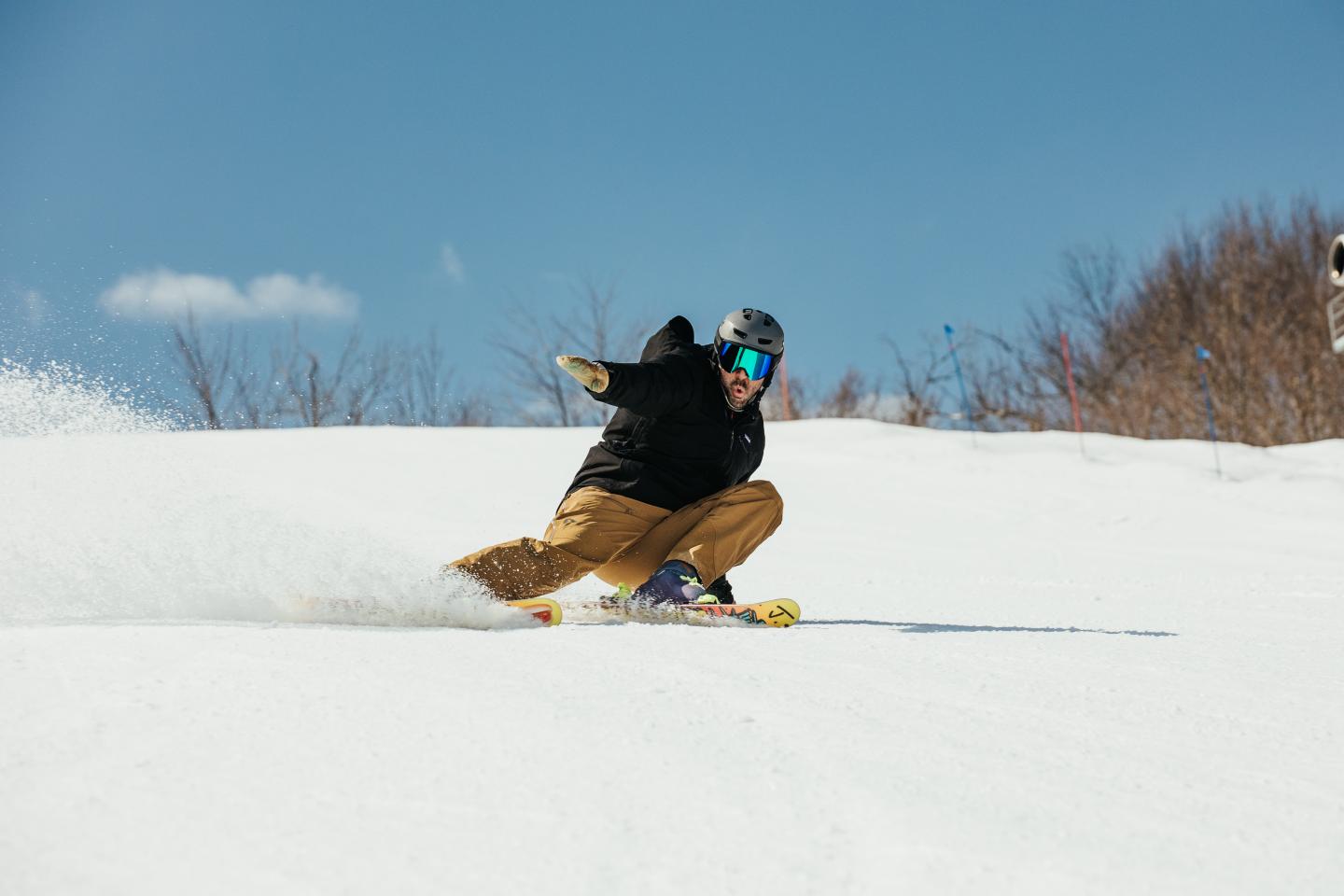 Skier in brown pants carving down a snowy slope under a clear blue sky.
