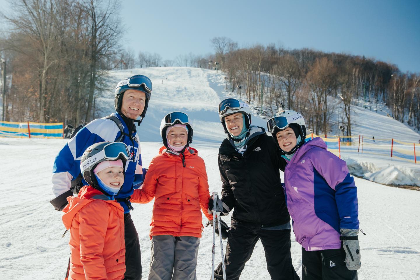 Family in ski gear posing on snowy slope, smiling.