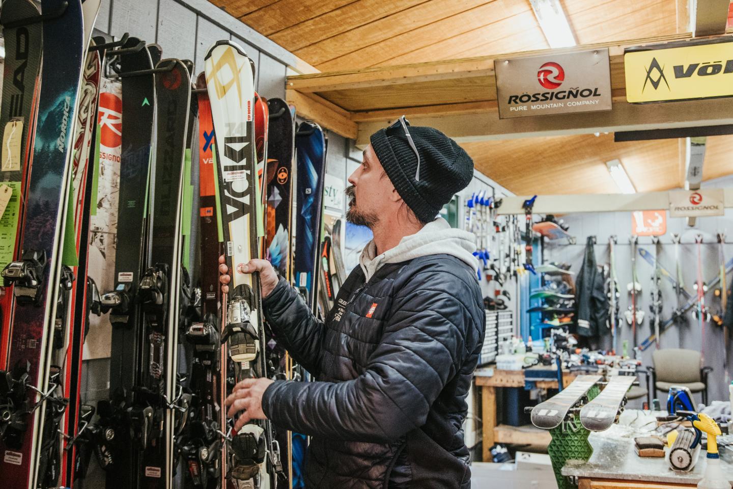 Man in a ski shop examining skis on a wall rack.