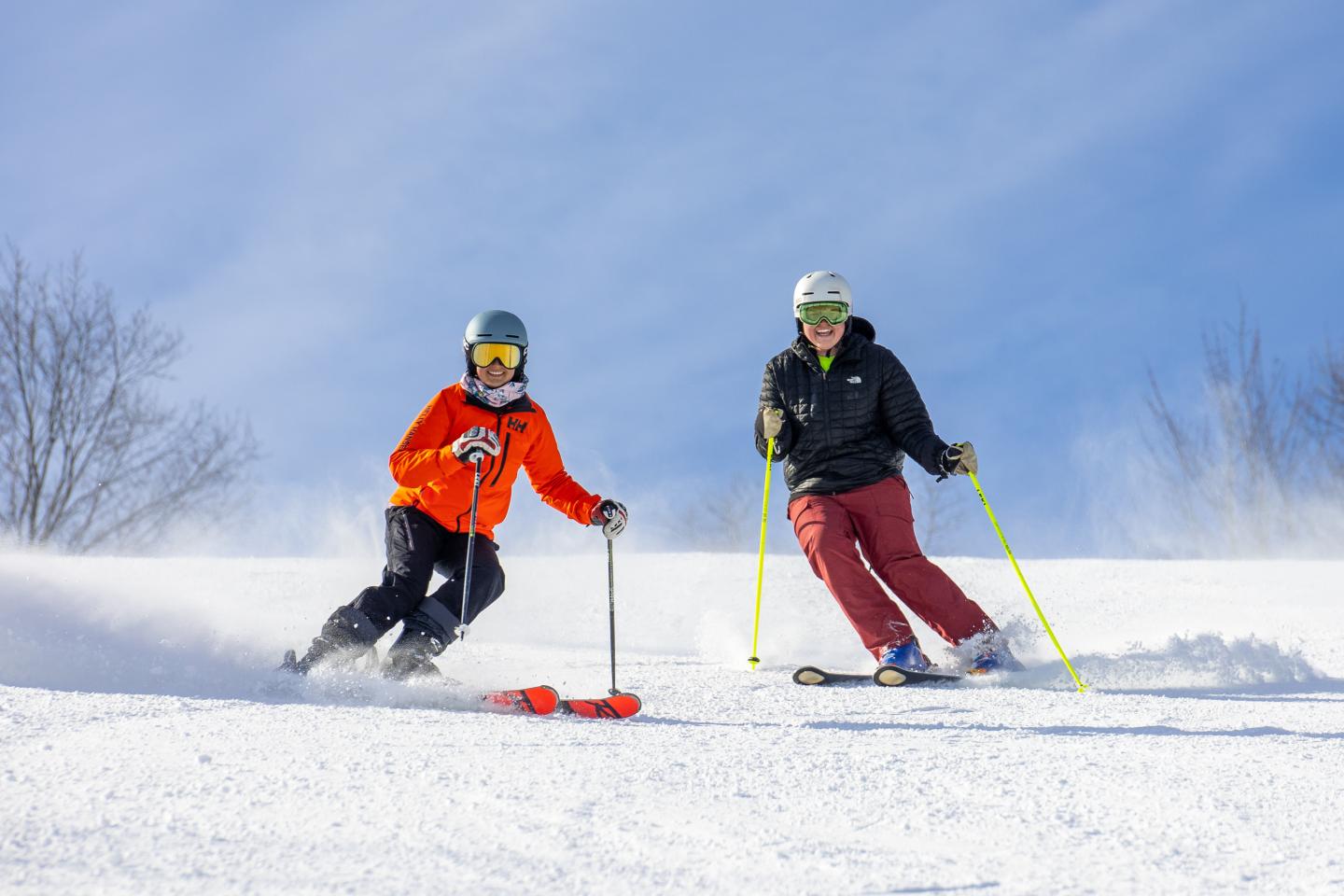 Two people skiing downhill on a sunny day.