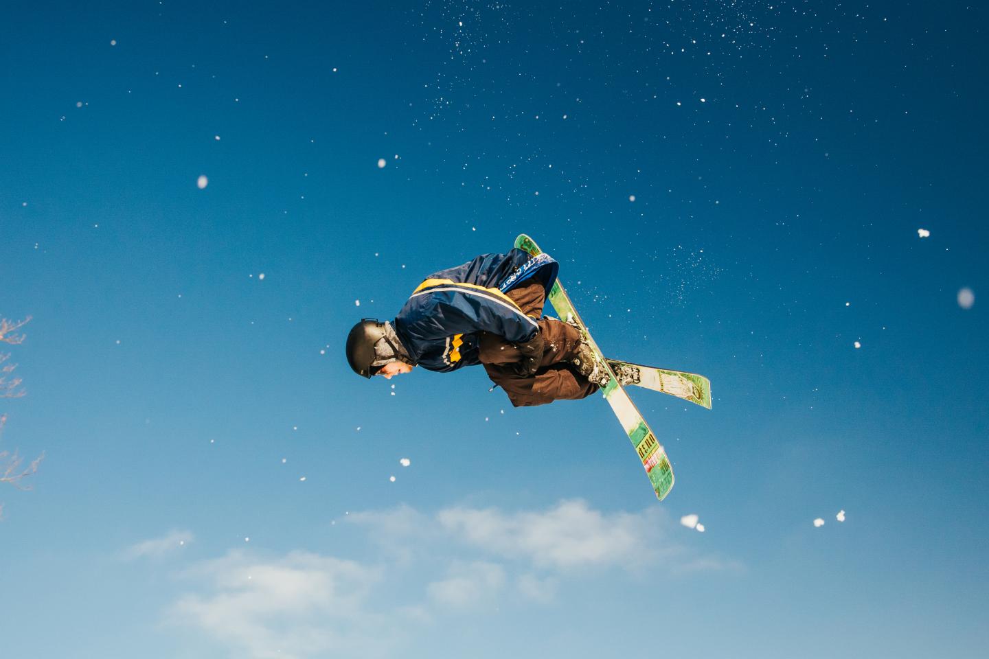 Skier midair against a clear blue sky, performing a trick.