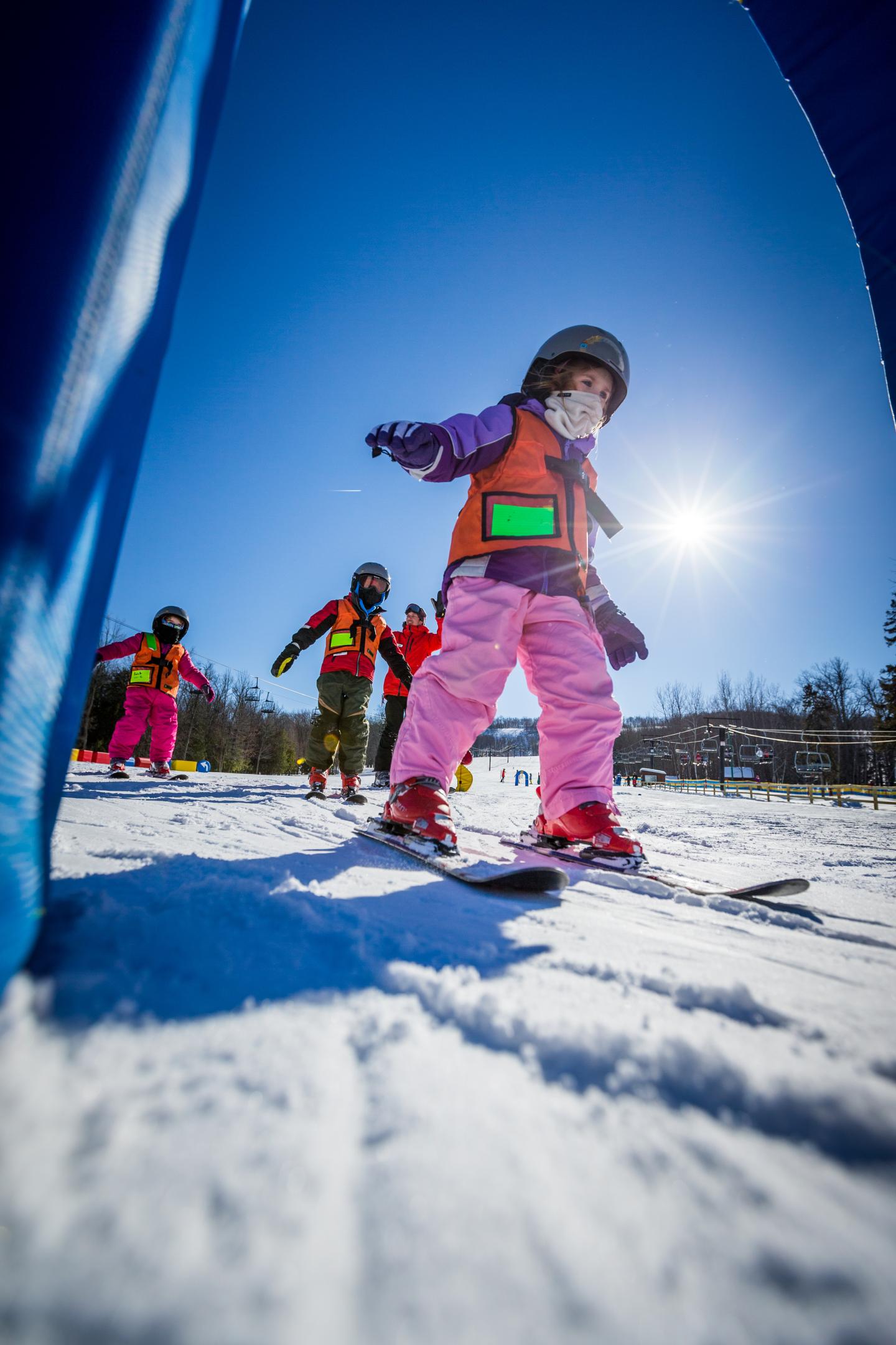 Child skiing downhill on a sunny day, wearing colorful winter gear.