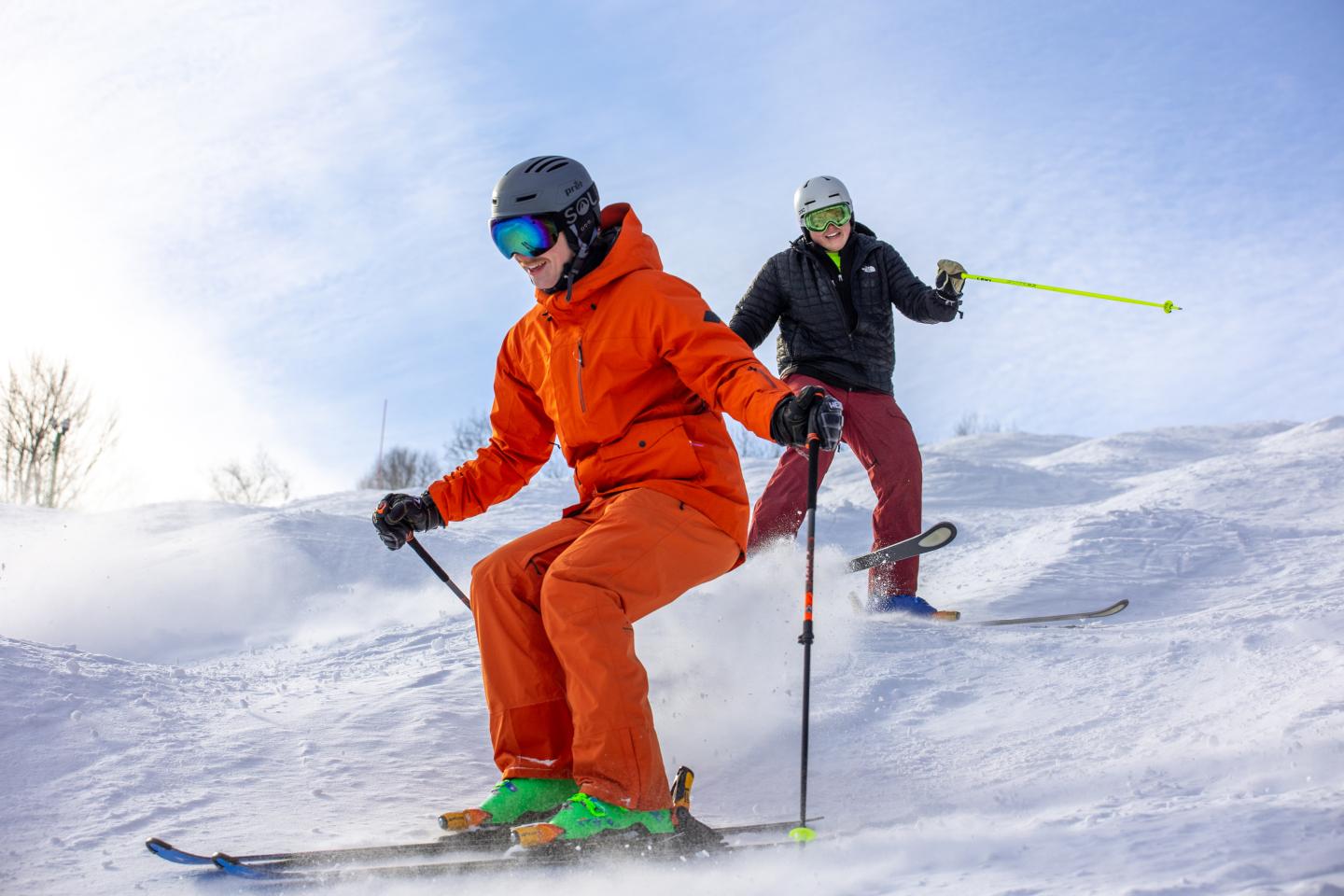 Two skiers in bright outfits glide down a snowy slope.