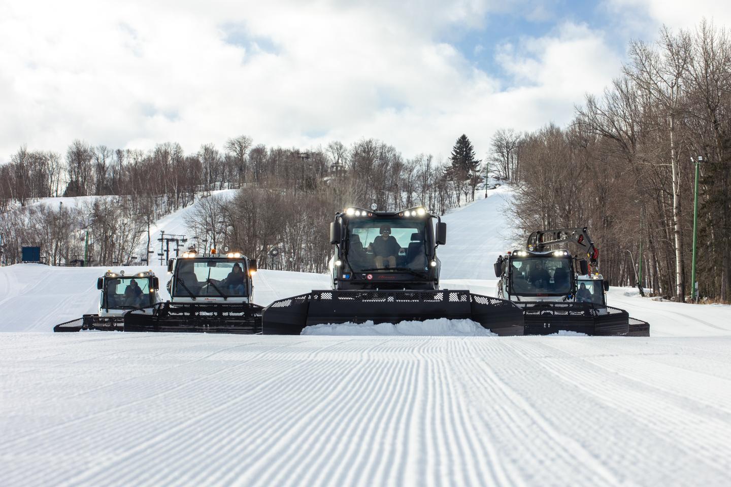 Three snow groomers lined up on a freshly groomed ski slope.