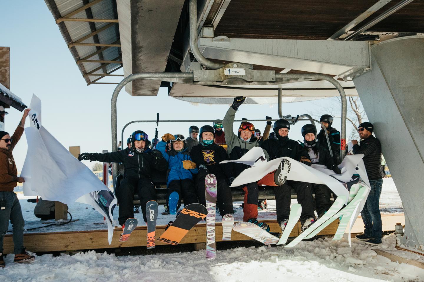 Group of people in winter clothing posing with snowboards in a damaged building.