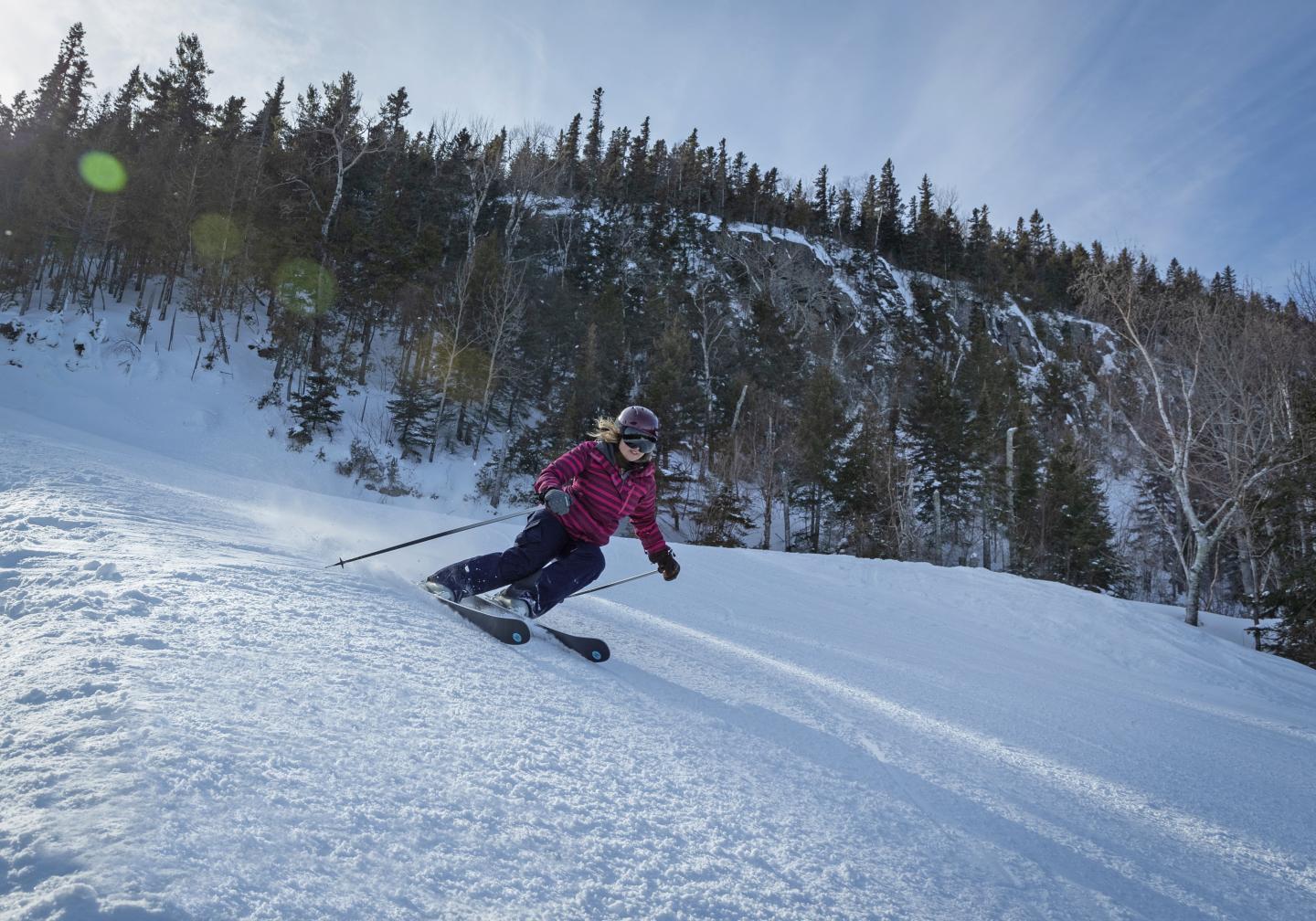 Skier in a pink jacket carving down a snowy mountain slope.